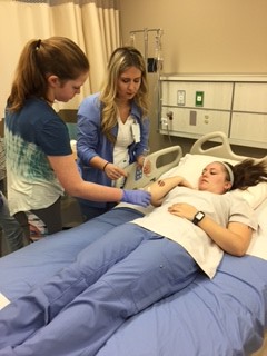 First-year student Mallory Drew instructs Girl Scout Ellie Davis about how to properly clean a wound on the arm of senior student Jessica DeFilippis. 