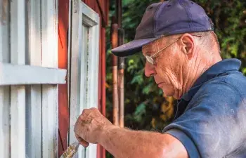 An older man painting a fence