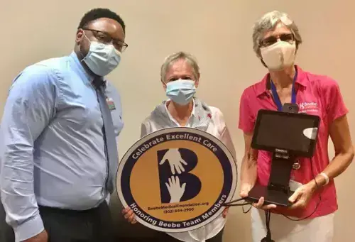 Kathee Brown celebrates the excellent care she received at Beebe Healthcare by donating a contactless temperature screening device. Shown are (l-r) Maurice Winkfield, Beebe Healthcare director of patient access; Brown; and Diane Barlow, Beebe Medical Foundation gift planning officer.
