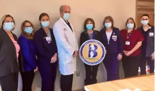 Alicia Beach (center, holding sign) celebrates excellent care at Beebe’s South Coastal Cancer Center with her care team, (l-r) Beebe Oncology Services Nurse Manager Ella-Mae Shupe, Registrar Gail Johnson, Nurse Jill Abbott, Dr. William Ryan, Nurse Michele Fletcher, CCA Brandi Denning, and Nurse Audrey Umschlag.